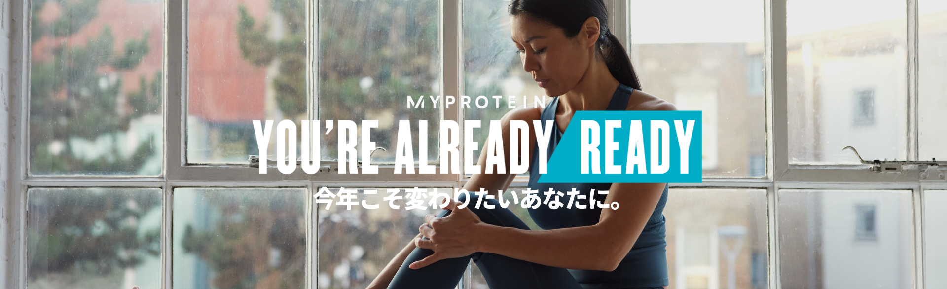 A woman wearing MP gym clothing sat on a window ledge stretching with the text 'You're Already Ready - MYPROTEIN' overlaying the image.